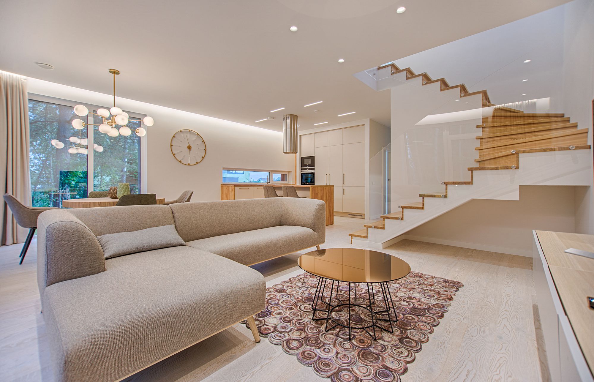 A professionally photographed living room with a linen sofa, oak staircase and open kitchen
